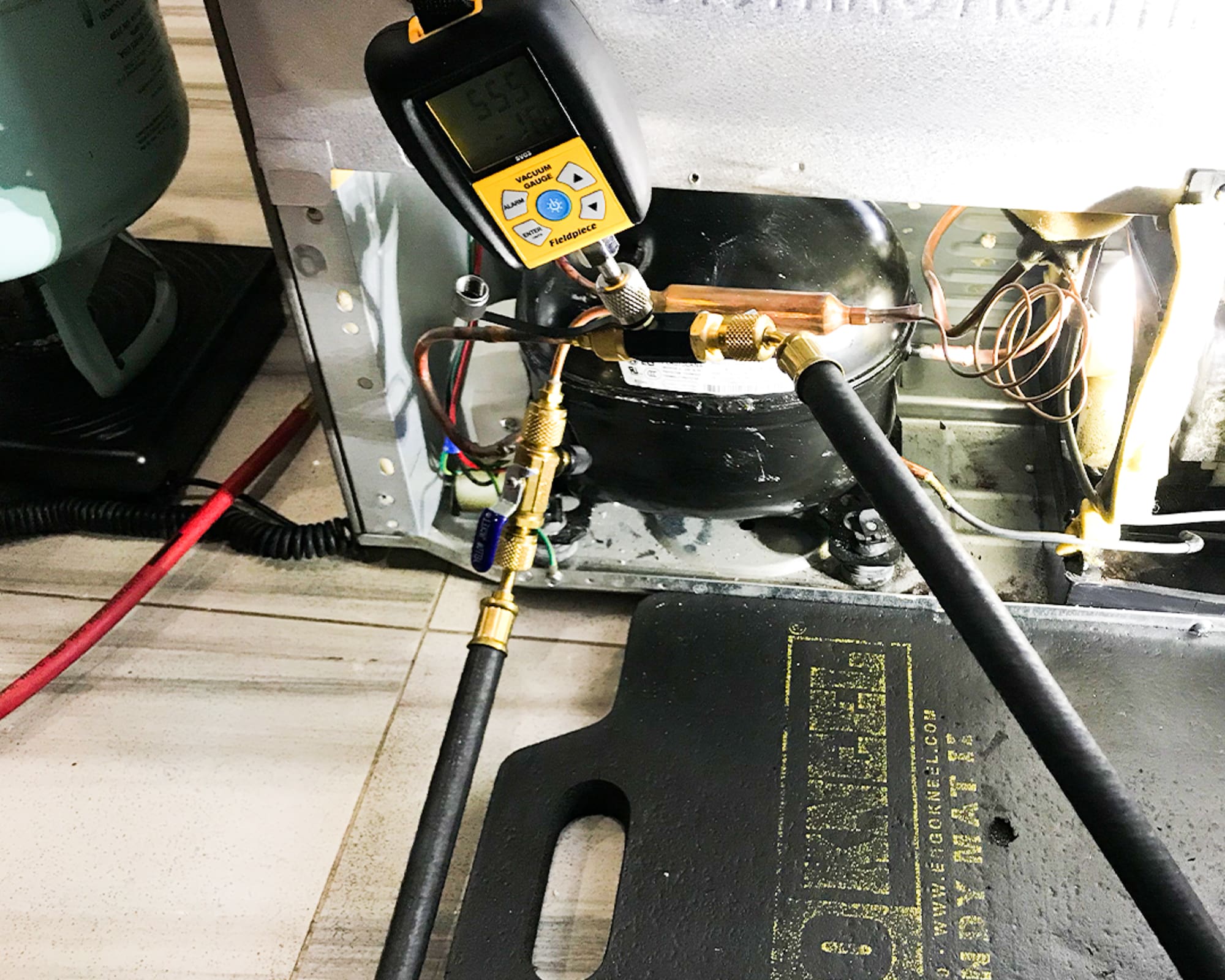 Appliance Repair man in action servicing a refrigerator - Micron gauge and vacuu